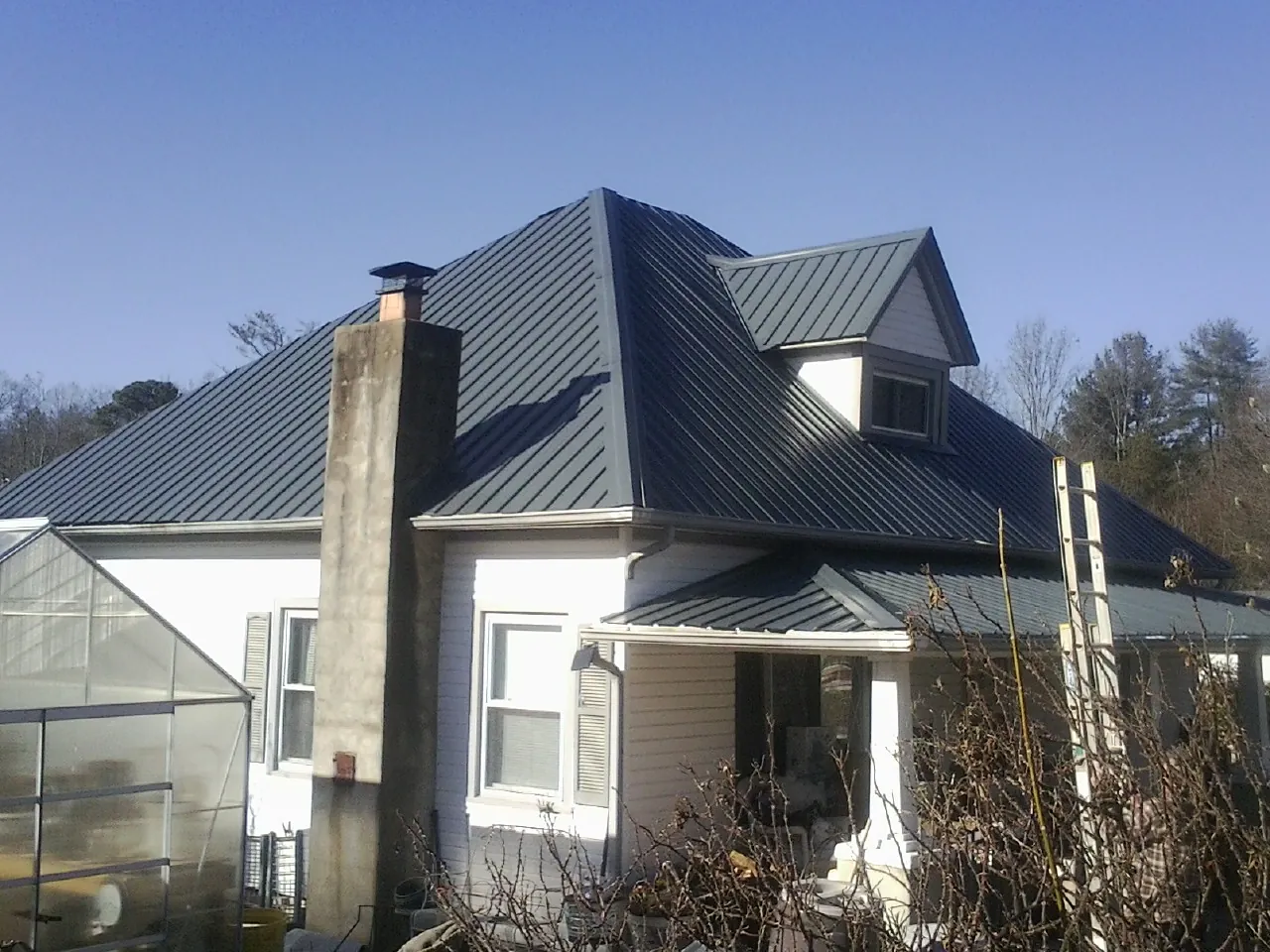 Dark blue standing seam metal roof on a white farmhouse with dormer — Slate & Tile Roof Repair by Roofing Brothers in Coldwater