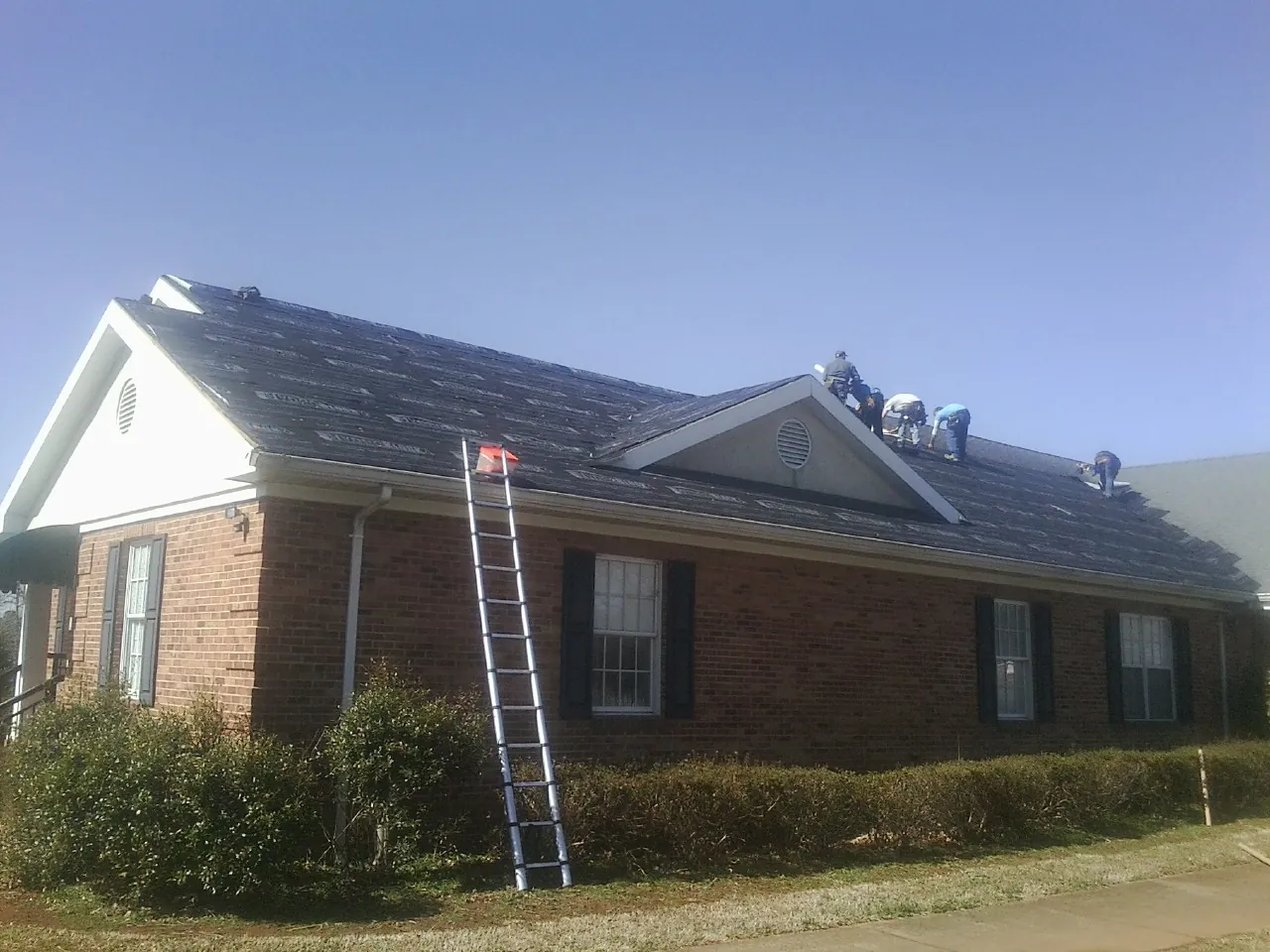 Crew tearing shingles off a brick ranch roof with a ladder set — Emergency Roof Repair work by our crew in Coldwater