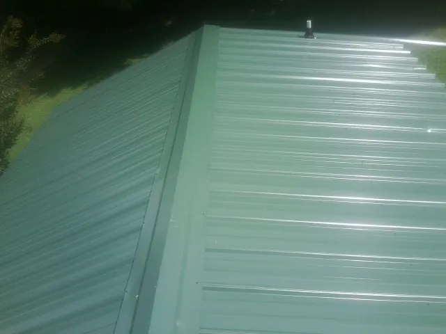 New green metal panels meeting at the ridge of a roof — Flat Roof Repair work by our crew in Coldwater