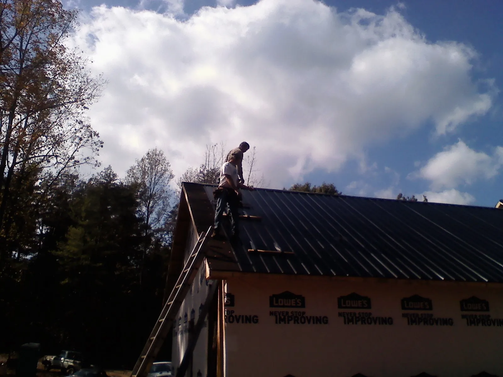 Roofer fastening dark metal panels high against a cloudy sky, from a Roof Inspection job in Coldwater