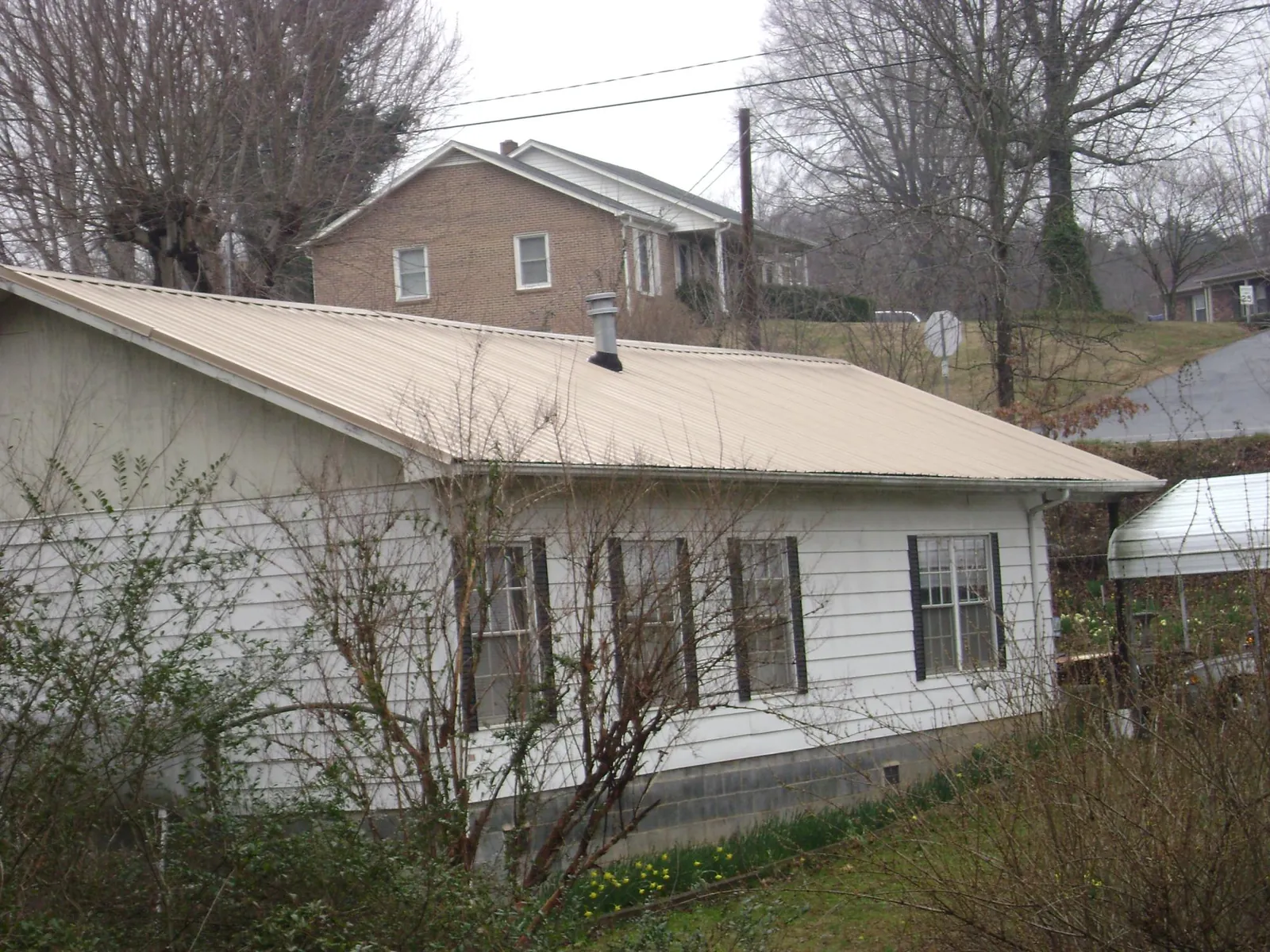 Tan metal roof on a white sided house set into a hillside — Commercial Roofing by Roofing Brothers in Coldwater